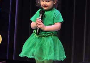 Dziewczynka w zielonym ubraniu śpiewa piosenkę o żabce.