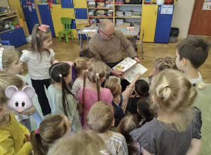 Dzieci słuchają radnego, który czyta wiersze.