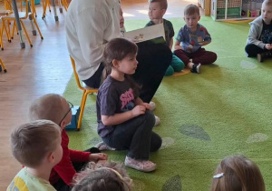 Dzieci słuchają radnego, który czyta wiersze.