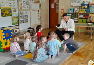 Dzieci słuchają radnego, który czyta wiersze.