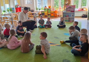 Dzieci słuchają radnego, który czyta wiersze.