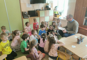 Dzieci słuchają radnego, który czyta wiersze.