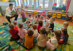 Dzieci słuchają radnego, który czyta wiersze.