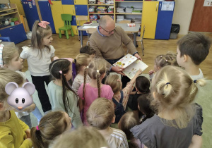 Dzieci słuchają radnego, który czyta wiersze.