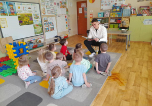 Dzieci słuchają radnego, który czyta wiersze.