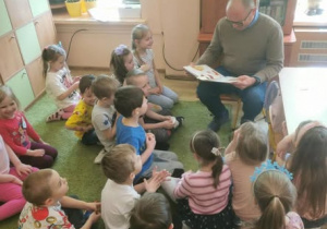 Dzieci słuchają radnego, który czyta wiersze.