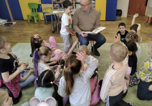 Dzieci słuchają radnego, który czyta wiersze.