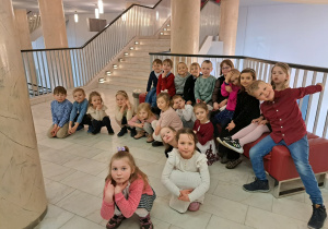 3 Grupa dzieci (część siedzi, część kuca) na korytarzu teatru przed wejściem na widownię