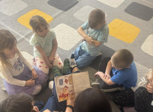 Dzieci siedzą na dywanie i słuchają opowiadań czytanych przez rodzica.