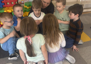 Dzieci siedzą na dywanie i słuchają opowiadań czytanych przez rodzica.