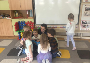 Dzieci siedzą na dywanie i słuchają opowiadań czytanych przez rodzica.