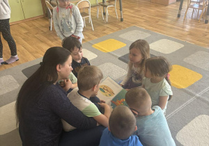 Dzieci siedzą na dywanie i słuchają opowiadań czytanych przez rodzica.