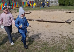 Dziewczynka i chłopiec biegną z cukierkami w stronę koszyka.