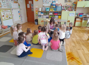 Grupa dzieci siedzi na dywanie i słucha czytanych przez rodzica bajek.