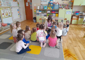 Grupa dzieci siedzi na dywanie i słucha czytanych przez rodzica bajek.