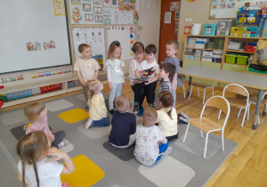 Grupa dzieci siedzi na dywanie i słucha czytanych przez rodzica bajek.