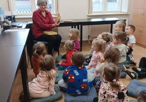 Dzieci siedzą na dywanie wpatrzone w panią bibliotekarkę