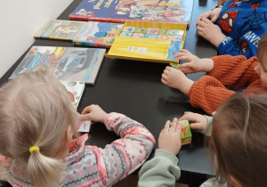 Maluszki stoją przy stole i oglądają ułożone na nich książki