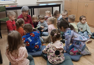 Dzieci siedzą wkoło bibliotekarki i słuchają czytanego opowiadania