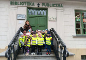 Grupa dzieci z nauczycielem stoi przy drzwiach Publicznej Biblioteki