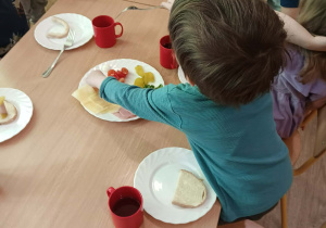 Dzieci siedzą przy stole i robią sobie samodzielnie kanapki