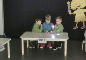 Grupa chłopców realizuje zadanie konkursowe podświetlając kartki latarką.