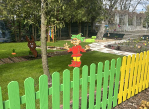 Kolorowy krasnoludek wykonany z drewna na kolorowym płotku.