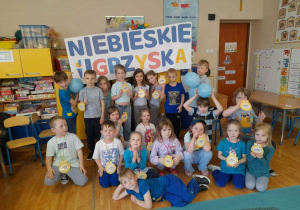 Grupa z najstarszej grupy przedszkolnej prezentuje medale, które otrzymała po zajęciach sportowych. Za nimi znajduje się baner „Niebieskie Igrzyska”.