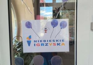 Informacja na drzwiach wejściowych przedszkola, mówiąca o tym, że placówka bierze udział w Niebieskich Igrzyskach.