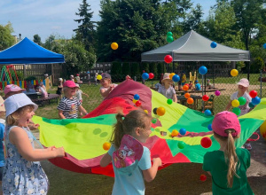 Grupa dzieci podczas zabawy z wykorzystaniem chusty animacyjnej i kolorowych piłeczek.