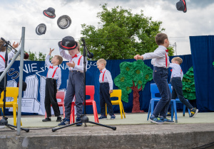 Grupa chłopców w trakcie tańca z użyciem krzeseł i kapeluszy.