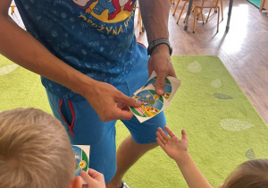 Prowadzący zajęcia sportowe rozdaje kolorowe naklejki dzieciom, które wyciągają po ręce