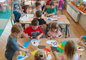 Dzieci wyklejają białe serduszka z papieru kolorowymi skrawkami wycinanki.