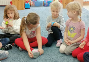 Dzieci siedzą na dywanie i trzymają w rękach sensoryczne baloniki