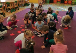 Dzieci w rozsypce siedzą na dywanie, na którym rozsypane są połówki różnej wielkości serc