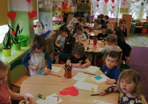Dzieci przy stolikach kolorują walentynkową kartkę