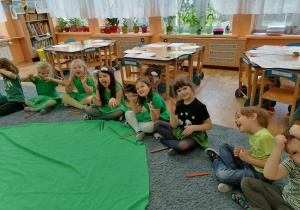 Dzieci siedzą na dywanie i pokazują miny Ufoludków.
