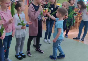 Chłopiec wręcza kwiaty dziewczynkom.