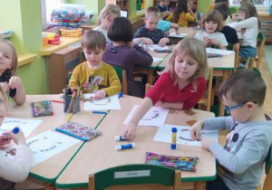 Dzieci przy stolikach kolorują i wyklejają kawałkami papieru podkowy.