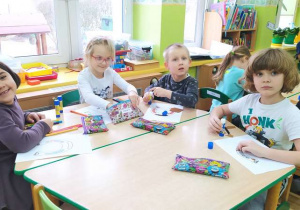 Dzieci przy stolikach kolorują i wyklejają kawałkami papieru podkowy.