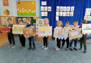 Dzieci ustawione w szeregu trzymają swoje prace - rysunkowe wagoniki.