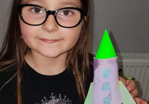 Dziewczynka pokazuje rakietę wykonaną z rolki papierowej.