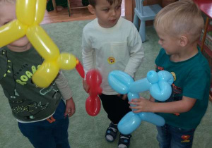 Trzech chłopców bawi się zwierzątkami wykonanymi z balonów.