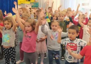 Grupa dzieci tańczy z uniesionymi rękami do góry.