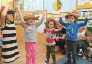 Troje dzieci tańczy w kapeluszach.