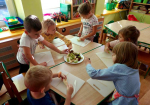 Dzieci siedzą przy stoliku i biorą owoce.