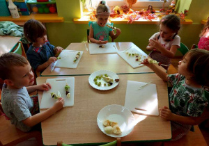 Dzieci przy stolikach jedzą owocowe szaszłyki.