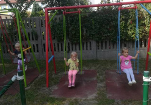 Dziewczynki w ogrodzie przedszkolnym huśtają się na huśtawce