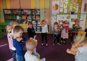Dzieci w kole trzymają w dłoniach misie i śpiewają piosenkę.