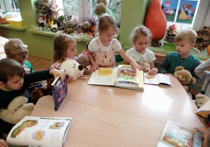 Dzieci siedzą przy stolikach i oglądają książki o misiach.